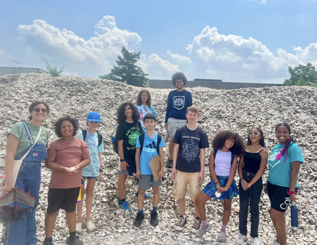 IndyKids + Billion Oyster Project’s Asly Ventura and Konner Wade Campbell Scheel stand on a giant pile of oyster shells.
